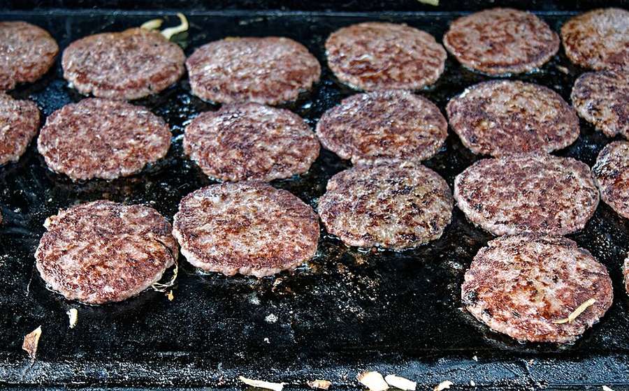 Rows of burger patties searing on a flat-top steel griddle